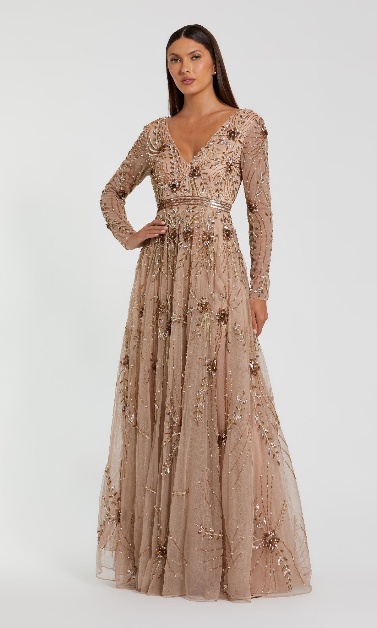 A woman models the Mac Duggal 6086 long sleeve beaded formal gown featuring intricate bead and sequin embellishments, sheer sleeves, and a deep V-neck, standing against a plain white background.